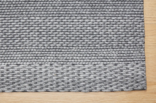 Albi Smoke is a Dark Grey and Black, PET Yarn (recycled Plastic) Hand woven rug. Sizes 160 X 230, 200 X 290 and 240 x 340. Corner.