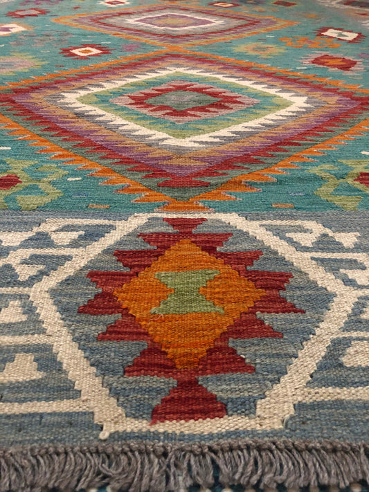 The Afghan Hand Woven Khyber Kilim - 197 X 304. Crafted using traditional vegetable dyed wool, and featuring traditional geometric designs. Colours, Greens, teals, blues, creams, reds, oranges and yellows. Size 197 X 304. Angle.