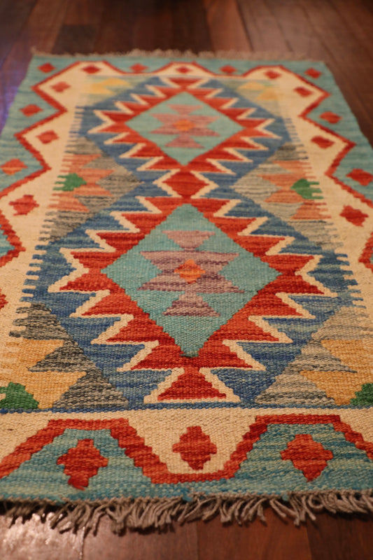 The Afghan Hand Woven Khyber Kilim - 58 X 88. Crafted using traditional vegetable dyed wool, and featuring traditional geometric designs. Colours, Dark oranges, creams, light greens, light blues yellows. Size 58 X 88. Angle.