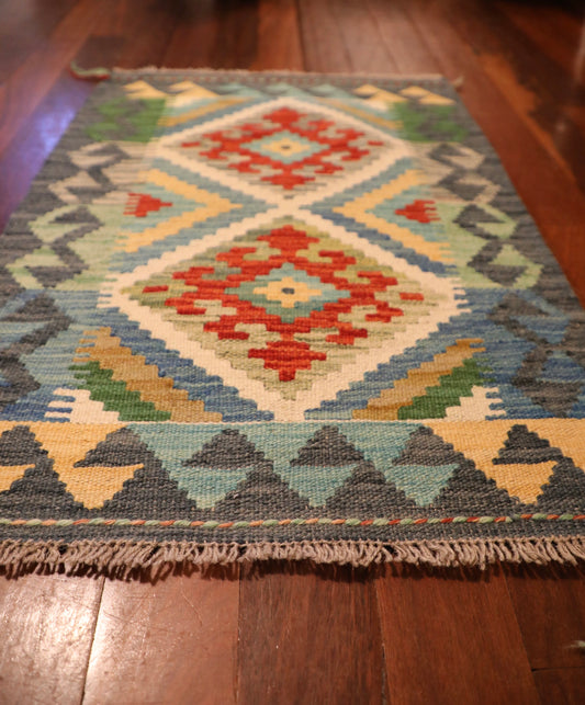 The Afghan Hand Woven Khyber Kilim - 60 X 88. Crafted using traditional vegetable dyed wool, and featuring traditional geometric designs. Colours, greys, creams, light blues, reds and orange. Size 60 wide X 88 length. Angle.