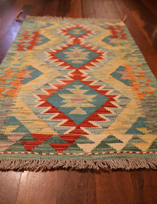The Afghan Hand Woven Khyber Kilim - 60 X 91. Crafted using traditional vegetable dyed wool, and featuring traditional geometric designs. Colours, Greens, beiges, yellows, creams, oranges, light blues. Size 60 X 91. Angle.