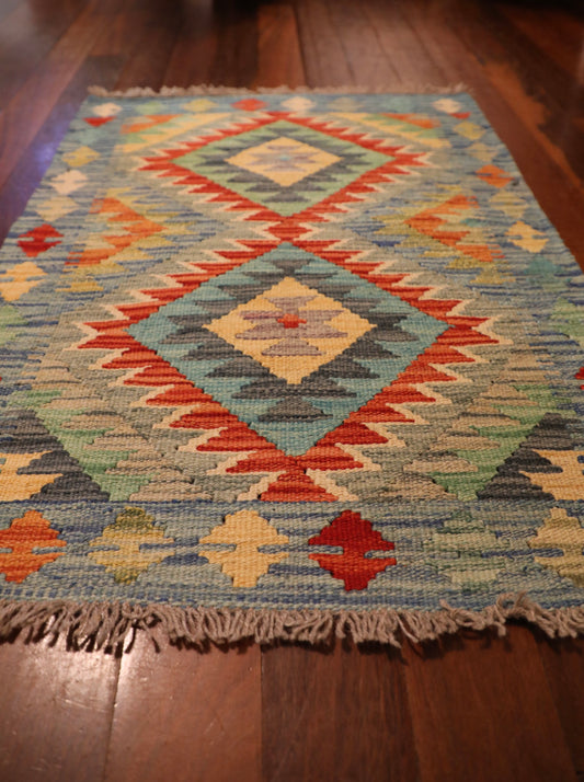 The Afghan Hand Woven Khyber Kilim - 64 X 86. Crafted using traditional vegetable dyed wool, and featuring traditional geometric designs. Colours, creams, light blues, reds and orange. Size 64 wide X 86 length. Angle.