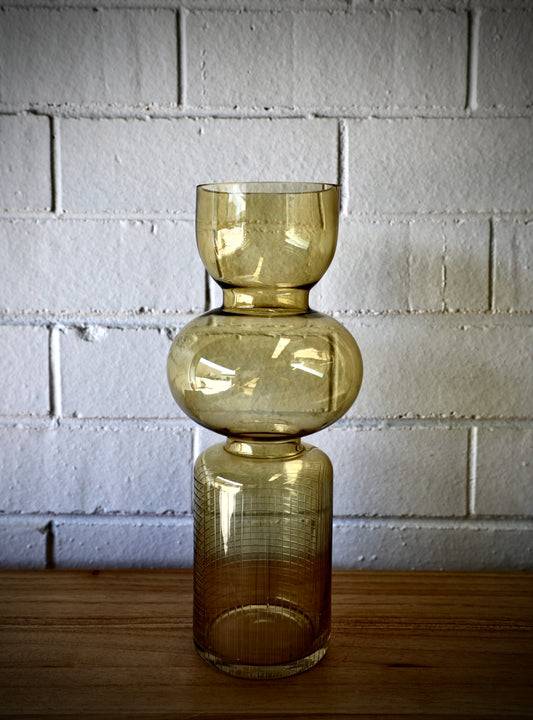 The Matar Glass Vase features a 3 column design. A cylindrical textured bottom, with bulbed middle and bowled open top. Colour Amber. Measures 13 Diameter X 30 Height. Plain.