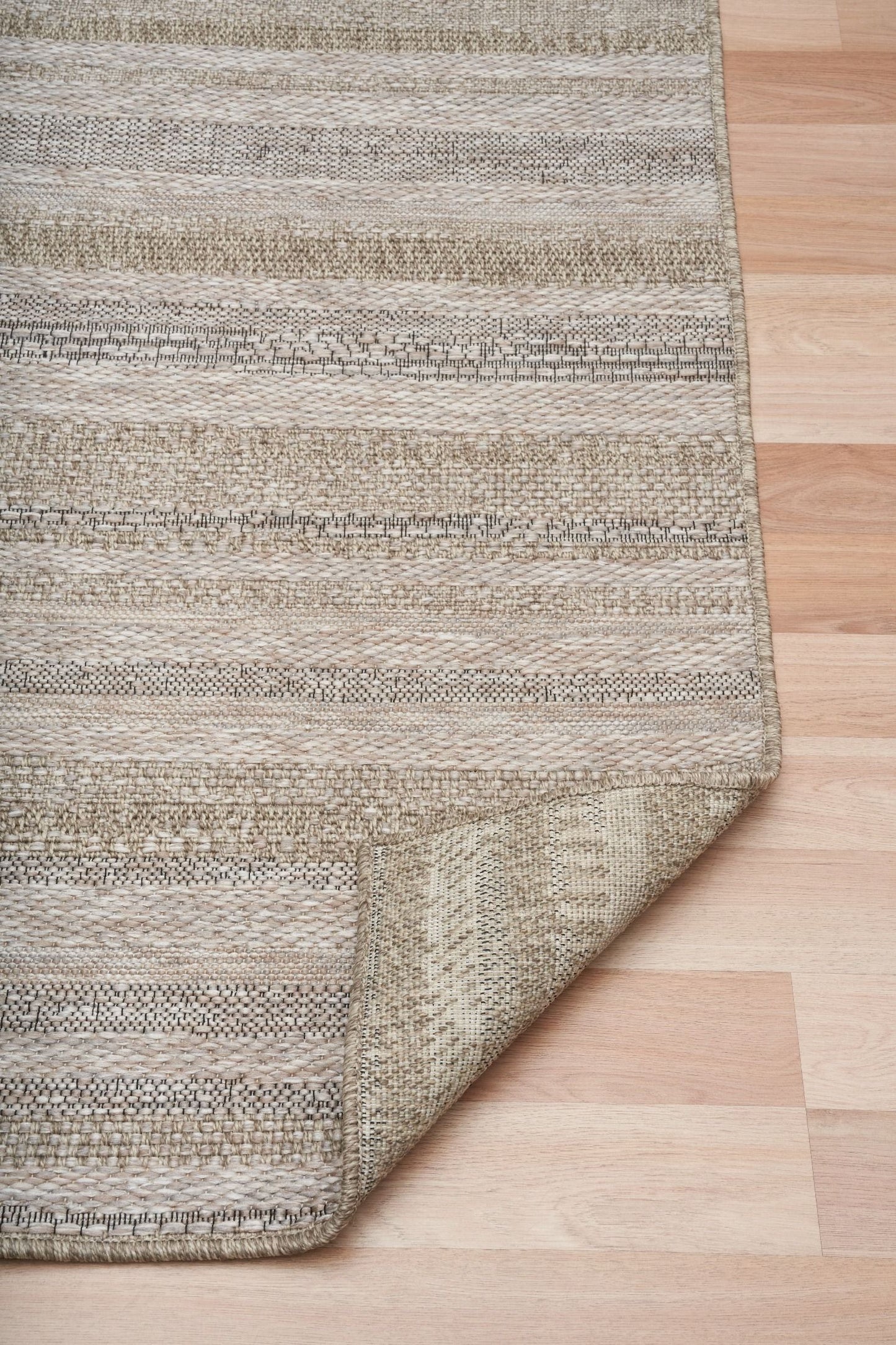 The Patio Linear Straw indoor/outdoor rug featuring neutral tones and a subtle textured pattern, power-loomed from UV-stabilised polypropylene for lasting durability. Colour Browns, Beiges and hints of black. 3 sizes. Fold.