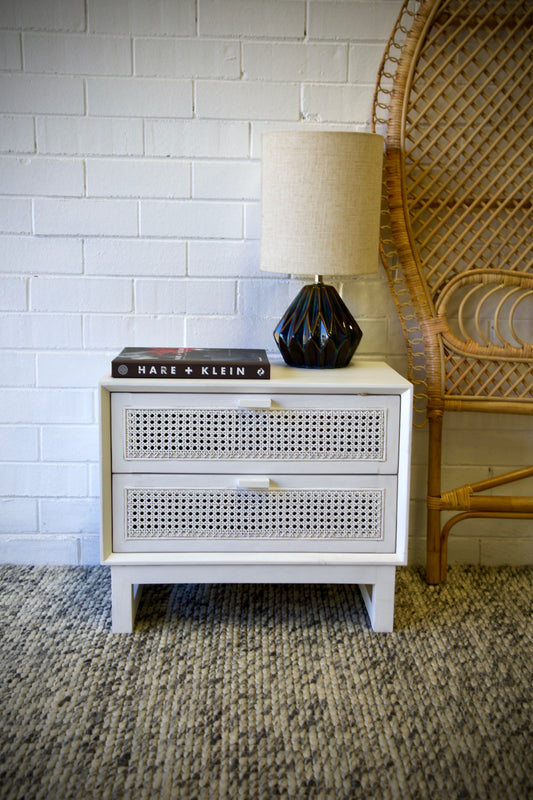 The Shasta 2 Drawer White Bedside offers a modern coastal aesthetic. Crafted from white cedar and rattan and featuring two drawers, on wood runners. Colour white. Measures 600 wide X 350 depth X 500 height. Front Styled.