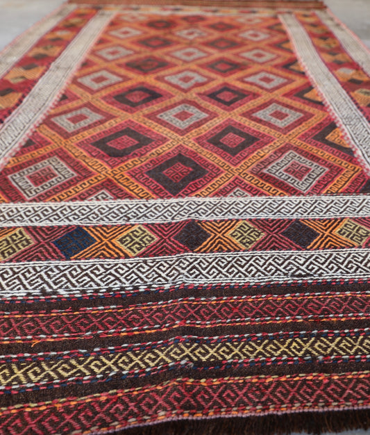 The Afghan Hand Woven Wool Suzani Kilim - 151 X 286. Hand woven by skilled afghan weavers, and featuring traditional bold geometric designs. Colours, oranges, reds, browns and creams. Measures 151 wide X 286 long. Angle.