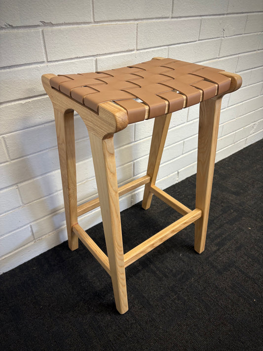 The Thames Barstool, tan leather, is designed with a contemporary style. Featuring a sustainable ash frame and a luxurious strapped saddle leather seat. Colour natural frame with tan leather. Measures 410 wide X 320 depth X 640 height. Angle.