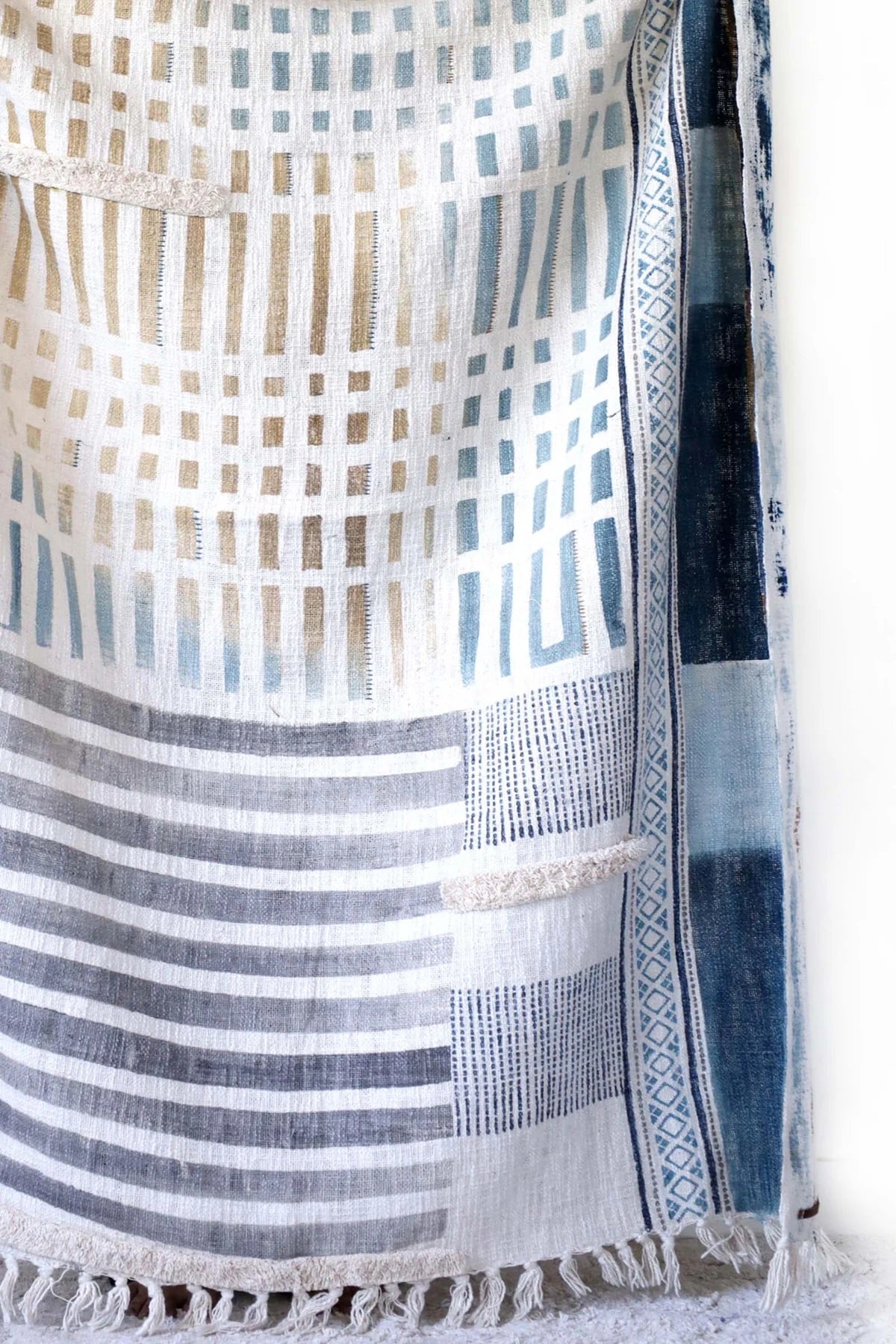 The Urbanic handcrafted throw blanket, adorned with a block print and playful tassels. Crafted from cotton slub from skilled artisans in India. It features a smooth textured feel. Indulge in the latest trend of Geometric Art with stunning shades of blue. Colours, blues, whites, beiges and greys. Size 130 X 170. Bottom corner.