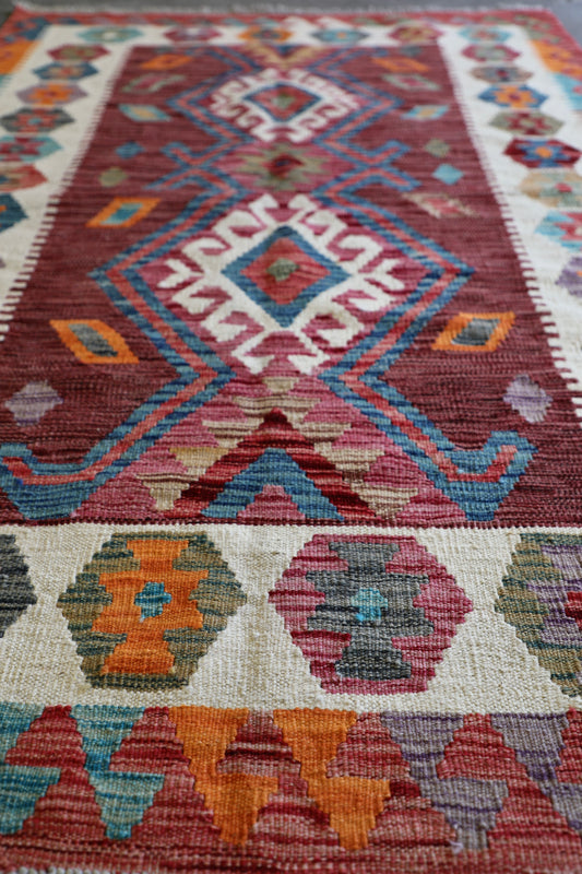 The Afghan Hand Woven Khyber Kilim 122 X 183. Crafted using traditional vegetable dyed wool, and featuring traditional geometric designs. Colours, reds, oranges, browns, creams and teal greens. Size 122 X 183. Angle.