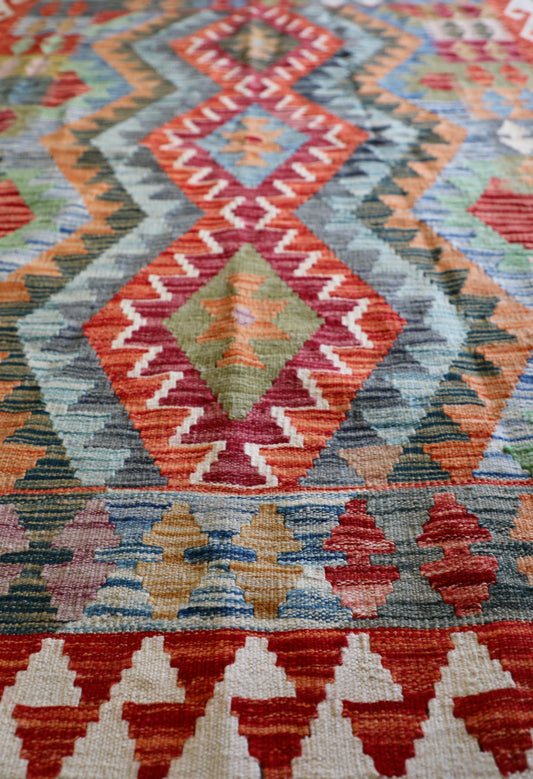 The Afghan Hand Woven Khyber Kilim - 124 X 178. Crafted using traditional vegetable dyed wool, and featuring traditional geometric designs. Colours, creams, oranges, greens and blues. Size 124 X 178. Angle.