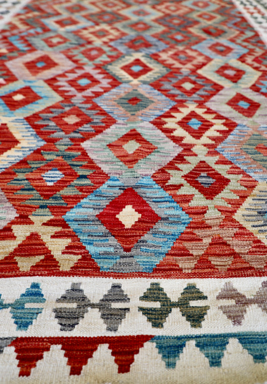 The Afghan Hand Woven Khyber Kilim - 184 X 250. Crafted using traditional vegetable dyed wool, and featuring traditional geometric designs. Colours, cream, reds, oranges, teals, yellows. Size 184 X 250. Angle.