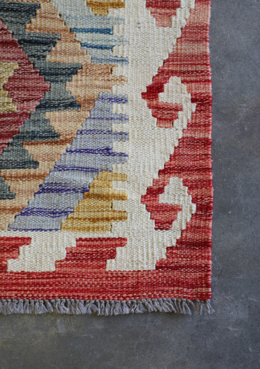 The Afghan Hand Woven Khyber Kilim - 62 X 92. Crafted using traditional vegetable dyed wool, and featuring traditional geometric designs. Colours, oranges, creams, light blues, dark greens. Size 62 X 92. Corner.