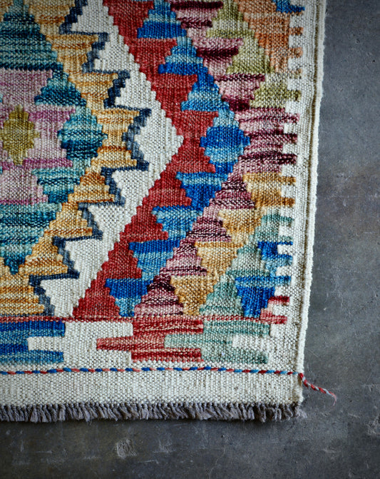 The Afghan Hand Woven Khyber Kilim 66 X 90. Crafted using traditional vegetable dyed wool, and featuring traditional geometric designs. Colours, creams, yellows, oranges, blue and dark greens. Size 66 X 90. Corner.