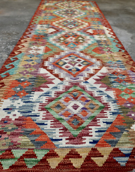 The Afghan Hand Woven Khyber Kilim Runner - 80 X 287. Crafted using traditional vegetable dyed wool, and featuring traditional geometric designs. Colours, Oranges, reds, yellow, teals and creams. Measures 80 wide X 287 long. Angle.