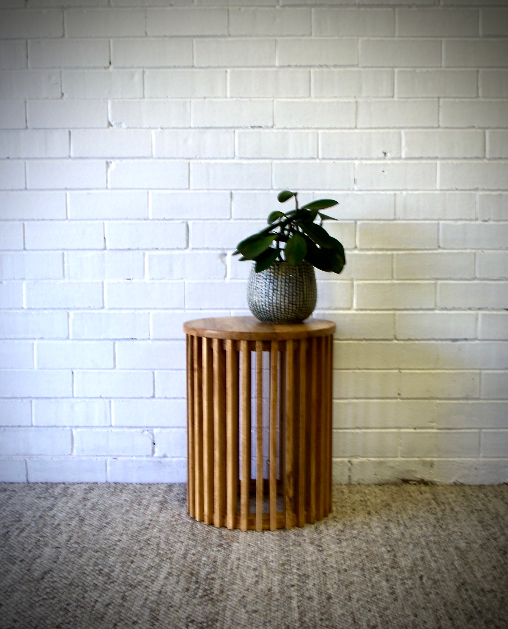  The Akashi Side Table, featuring a round top with slated sides crafted from sustainable fruitwood. Measures 400 diameter X 500 height. Styled.