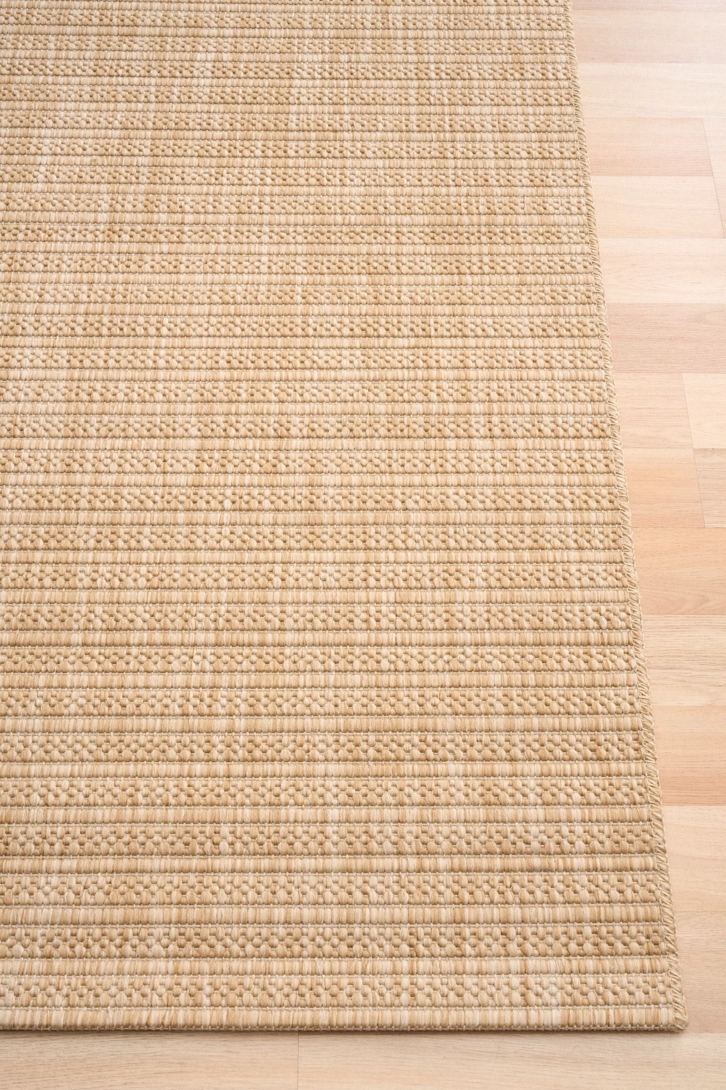Barton Linear Beige indoor/outdoor rug featuring soft beige tones and a subtle textured pattern, power-loomed from UV-stabilised polypropylene for lasting durability. Colour Beige. 3 sizes. Corner.