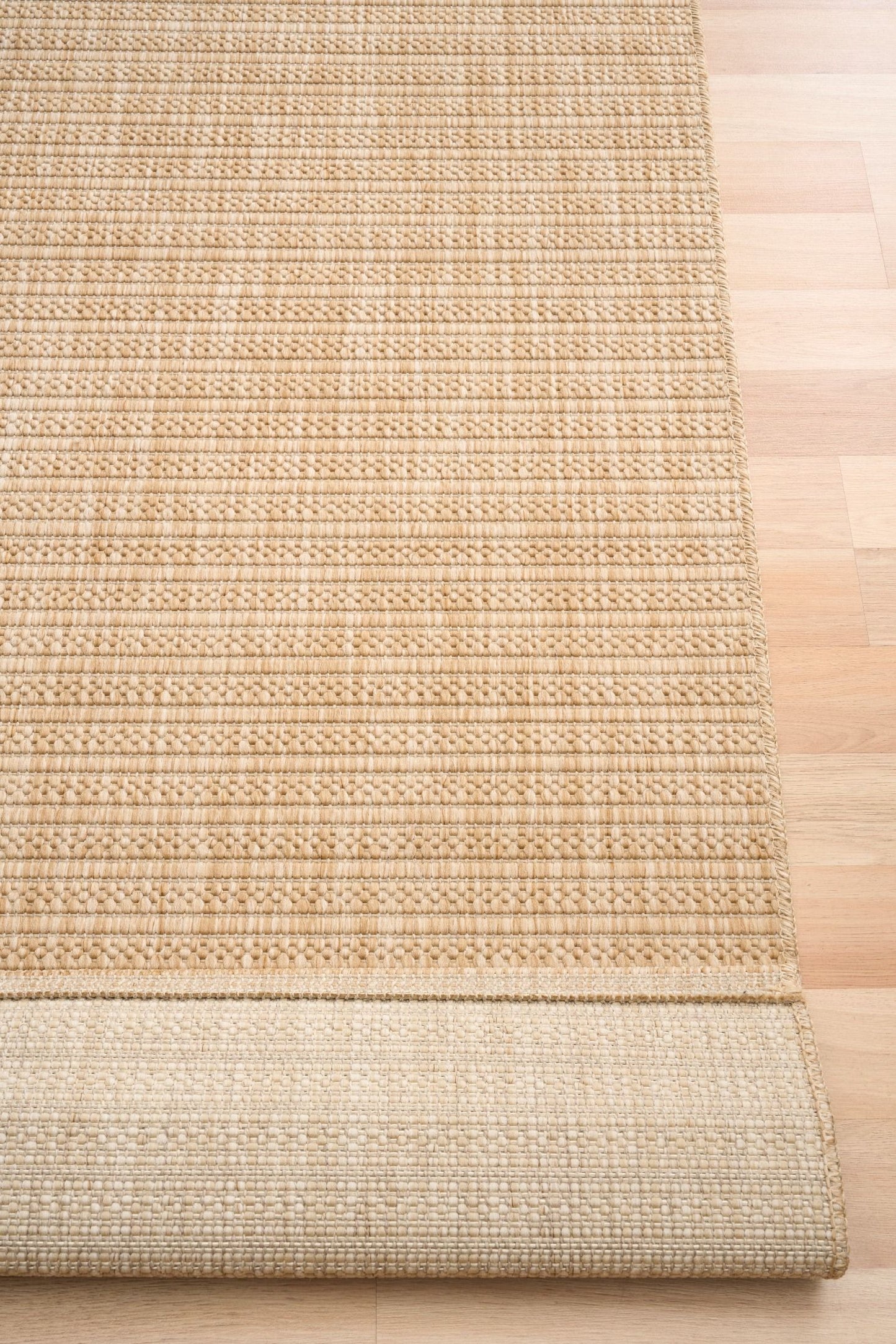 Barton Linear Beige indoor/outdoor rug featuring soft beige tones and a subtle textured pattern, power-loomed from UV-stabilised polypropylene for lasting durability. Colour Beige. 3 sizes. Fold.