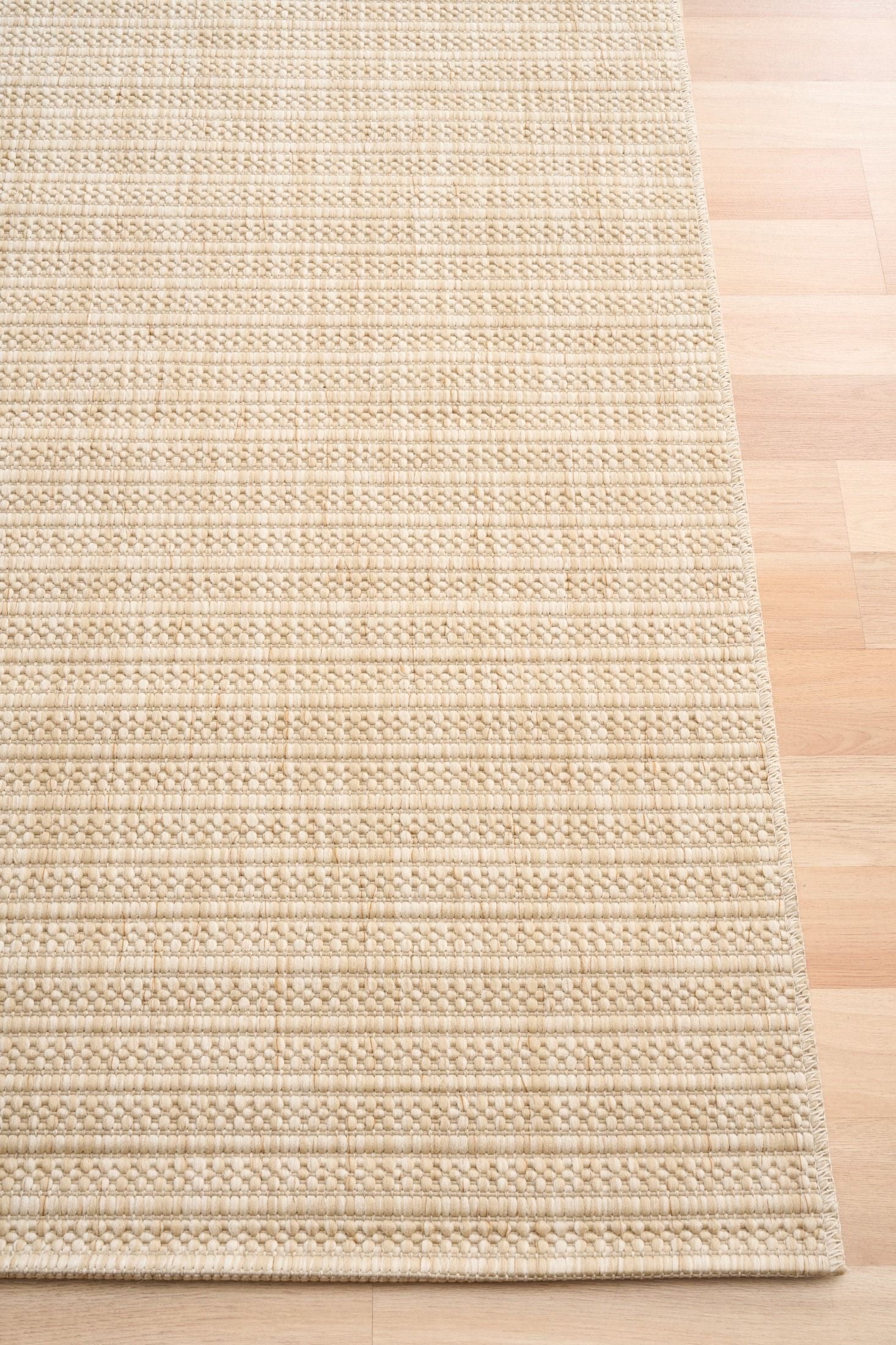 Barton Linear Cream indoor/outdoor rug featuring soft cream tones and a subtle textured pattern, power-loomed from UV-stabilised polypropylene for lasting durability. Colour Cream. 3 sizes. Corner.