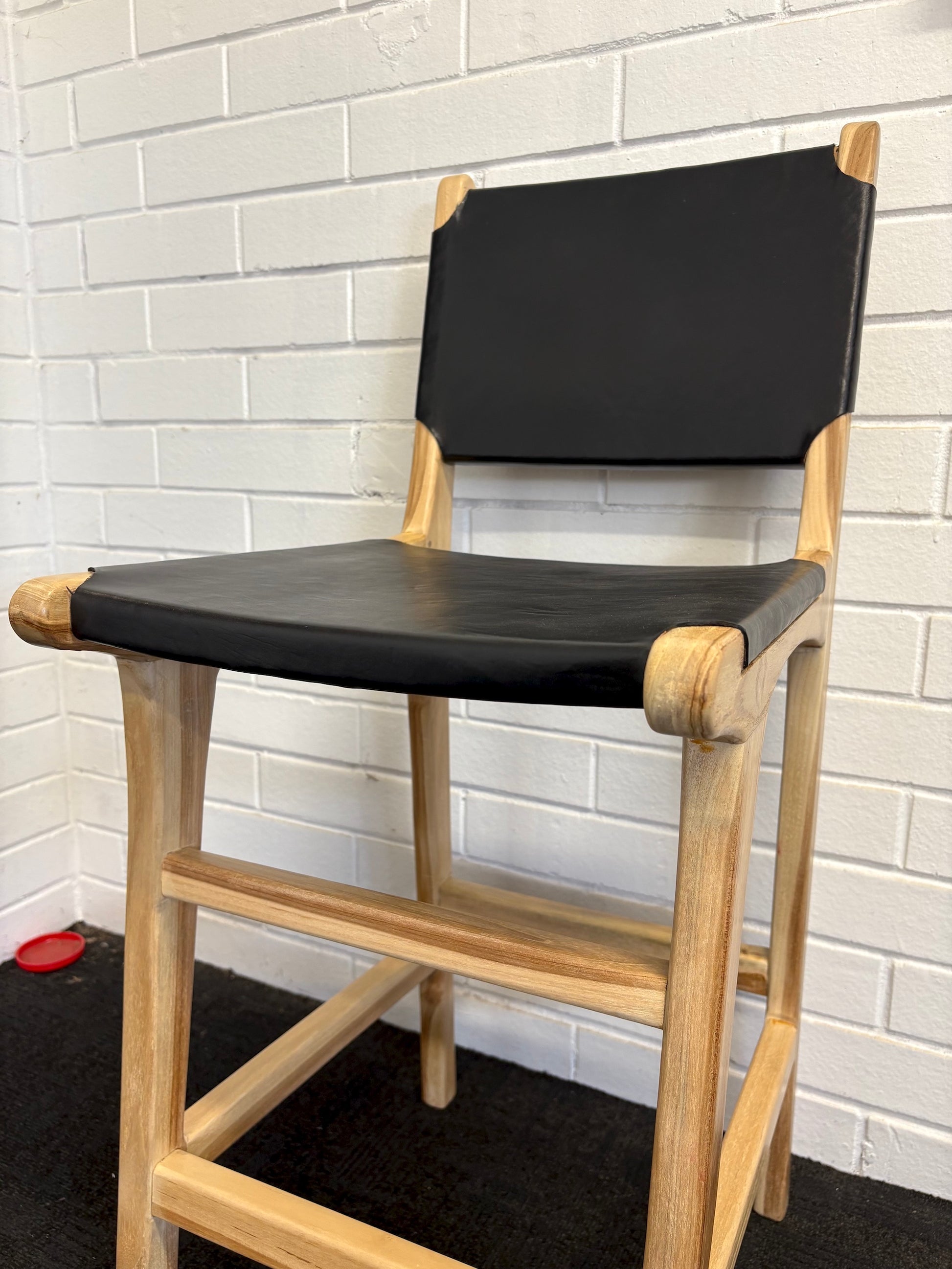 The Columbia with Back - Black Leather barstool features a black leather seat and back with sustainable teak framed legs. Colour natural teak frame with black leather seat and back. Measures 400 wide X 400 depth X 680 Seat height X 1000 Back height. Angle.