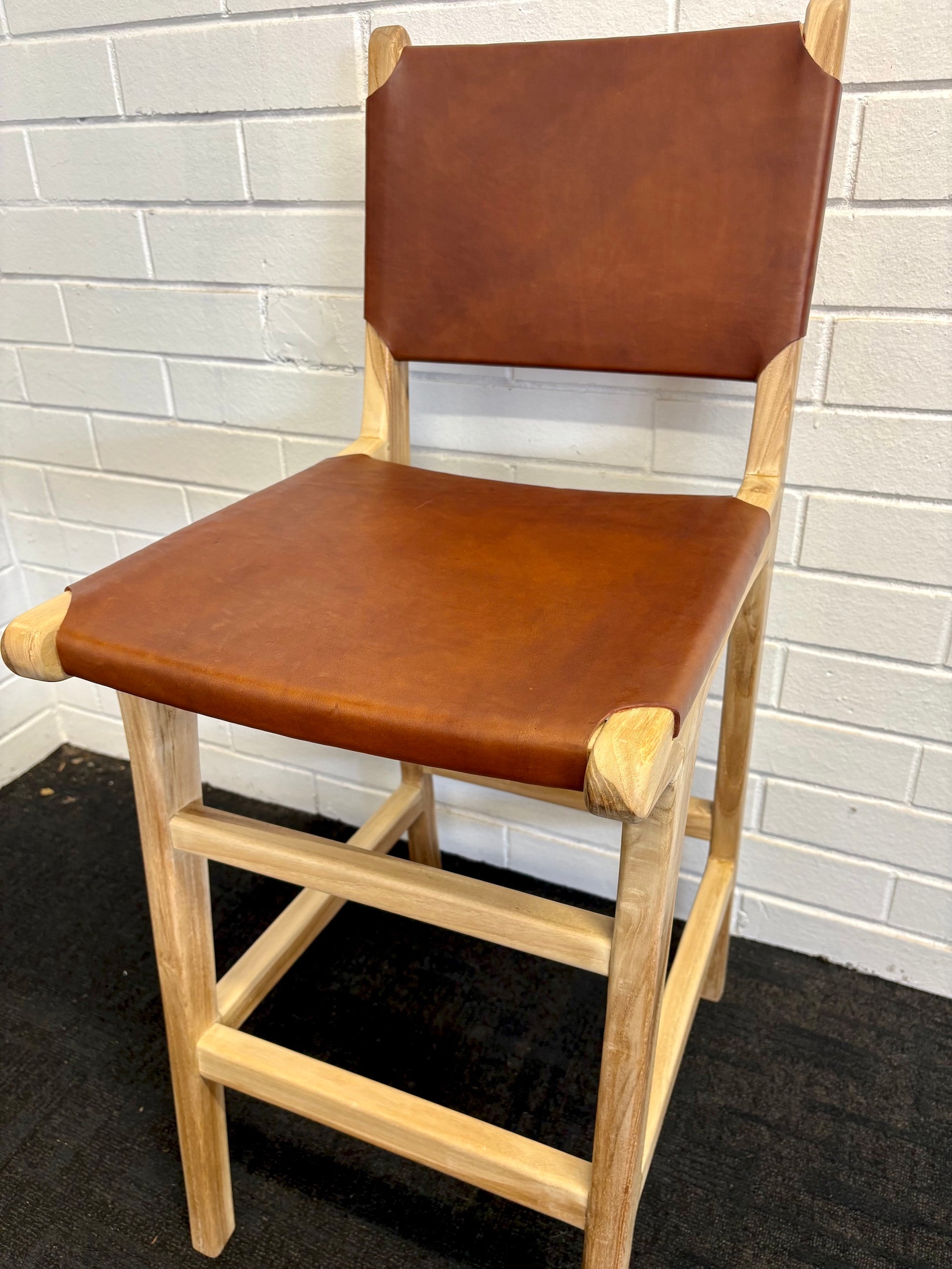 The Columbia with Back - Brown Leather barstool features a black leather seat and back with sustainable teak framed legs. Colour natural teak frame with brown leather seat and back. Measures 400 wide X 400 depth X 680 Seat height X 1000 Back height.  Angle.