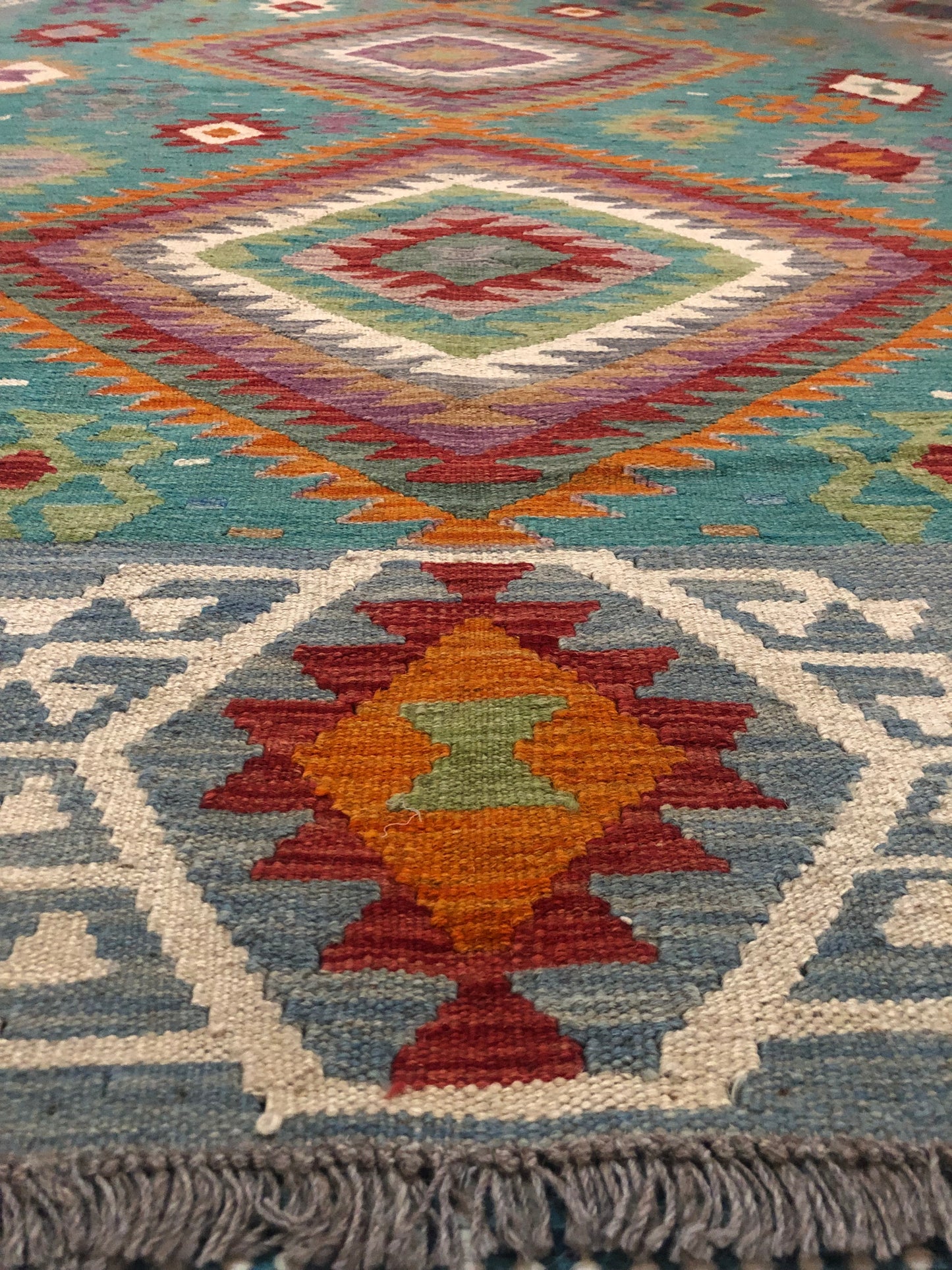 The Afghan Hand Woven Khyber Kilim - 197 X 304.  Crafted using traditional vegetable dyed wool, and featuring traditional geometric designs. Colours, Greens, teals, blues, creams, reds, oranges and yellows. Size 197 X 304. Angle.