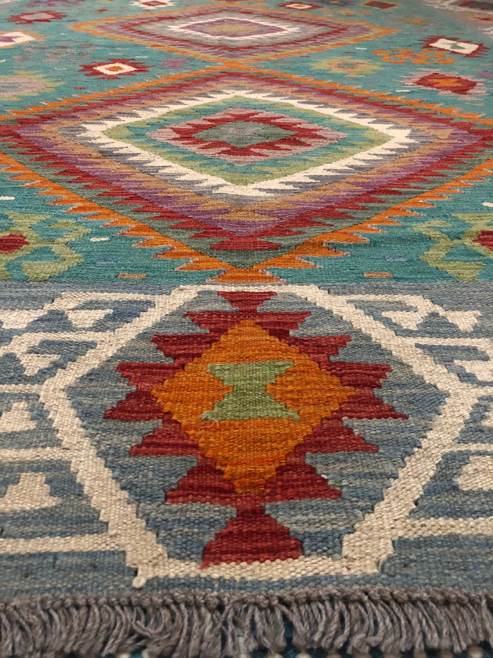 The Afghan Hand Woven Khyber Kilim - 197 X 304.  Crafted using traditional vegetable dyed wool, and featuring traditional geometric designs. Colours, Greens, teals, blues, creams, reds, oranges and yellows. Size 197 X 304. Angle.