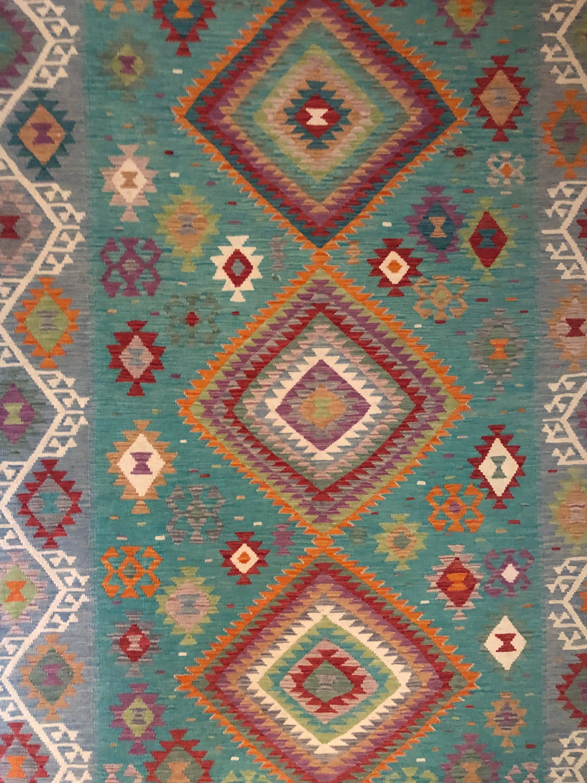 The Afghan Hand Woven Khyber Kilim - 197 X 304.  Crafted using traditional vegetable dyed wool, and featuring traditional geometric designs. Colours, Greens, teals, blues, creams, reds, oranges and yellows. Size 197 X 304. Top.