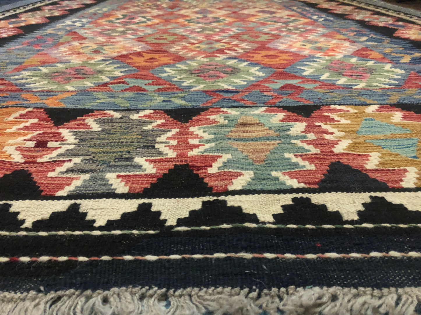 The Afghan Hand Woven Khyber Kilim - 202 X 290.  Crafted using traditional vegetable dyed wool, and featuring traditional geometric designs. Colours, blacks, blues, creams, reds, oranges and yellows. Size 202 X 290. Angle.
