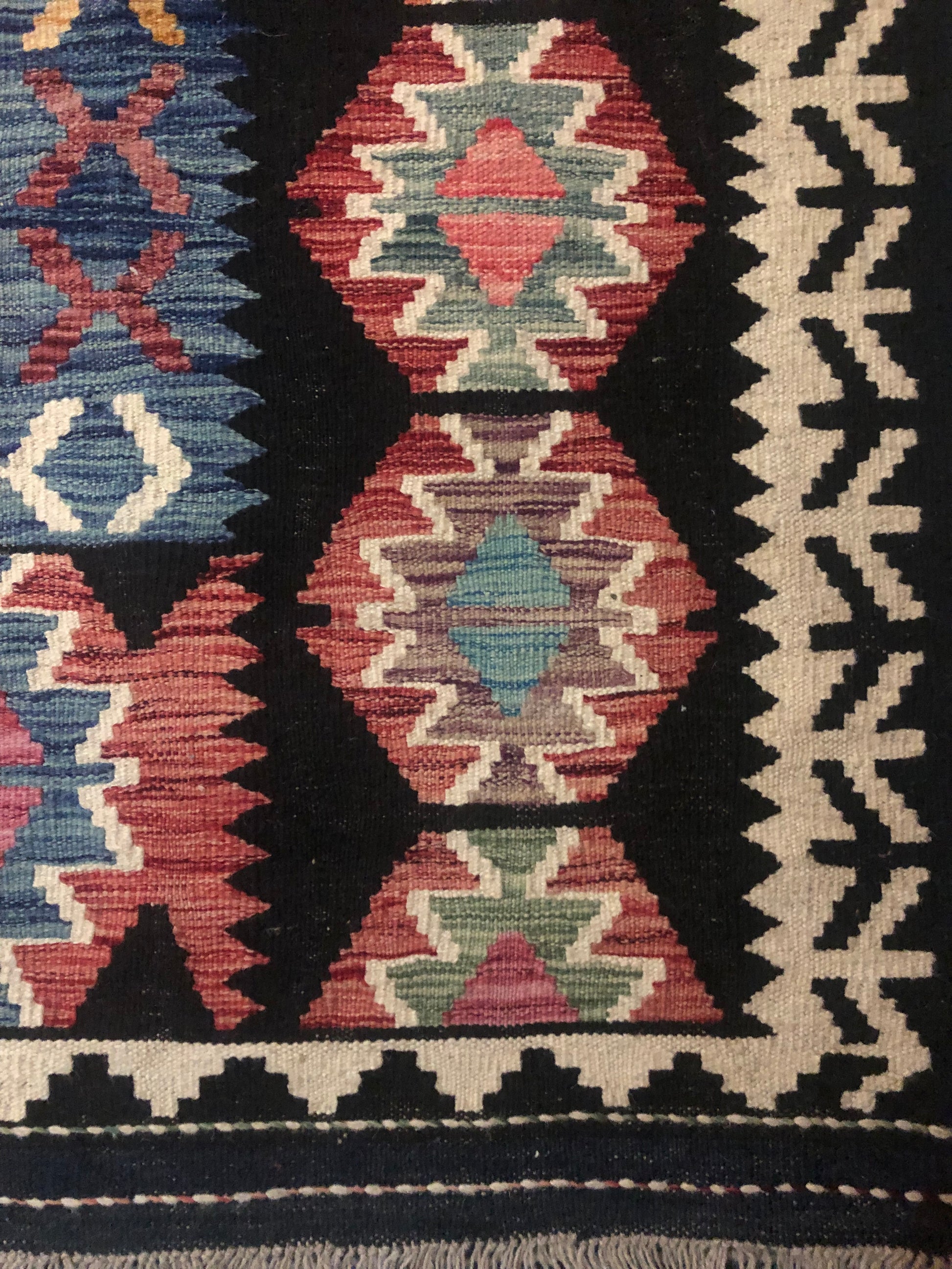 The Afghan Hand Woven Khyber Kilim - 202 X 290.  Crafted using traditional vegetable dyed wool, and featuring traditional geometric designs. Colours, blacks, blues, creams, reds, oranges and yellows. Size 202 X 290. Corner.