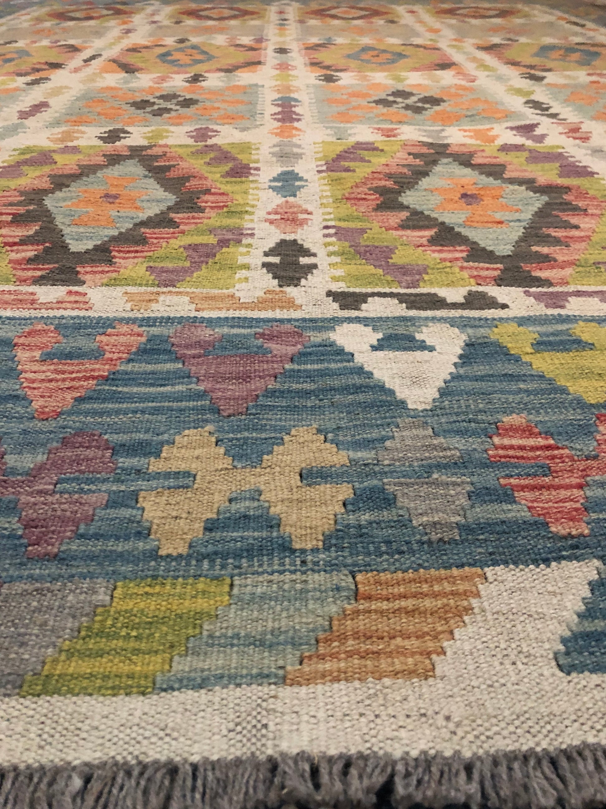 The Afghan Hand Woven Wool Khyber Kilim - 215 X 289. Crafted using traditional vegetable dyed wool, and featuring traditional geometric designs. Colours, greens, brown, cream, oranges, teals. Size 215 X 289. Angle.