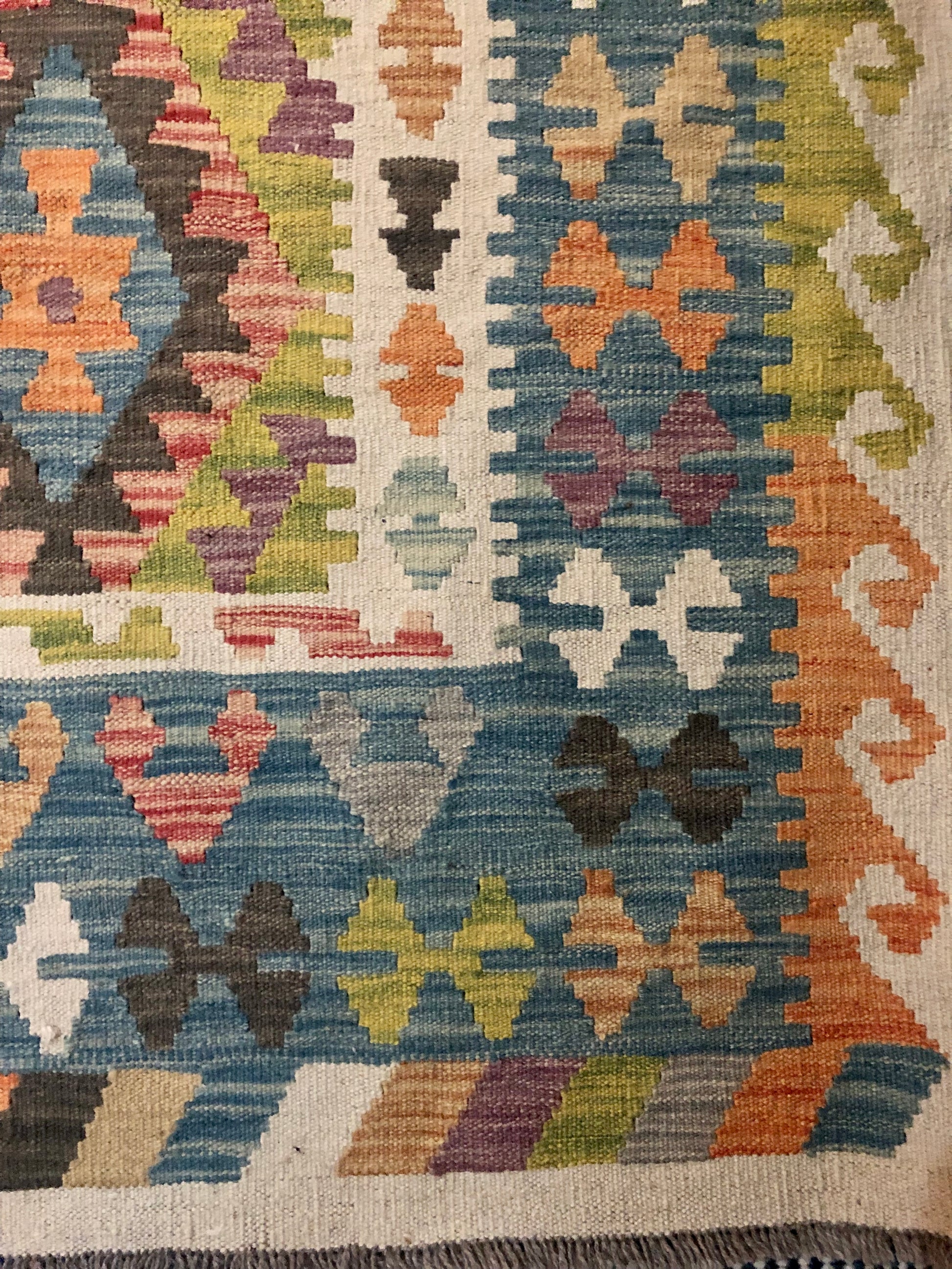 The Afghan Hand Woven Wool Khyber Kilim - 215 X 289. Crafted using traditional vegetable dyed wool, and featuring traditional geometric designs. Colours, greens, brown, cream, oranges, teals. Size 215 X 289. Corner.