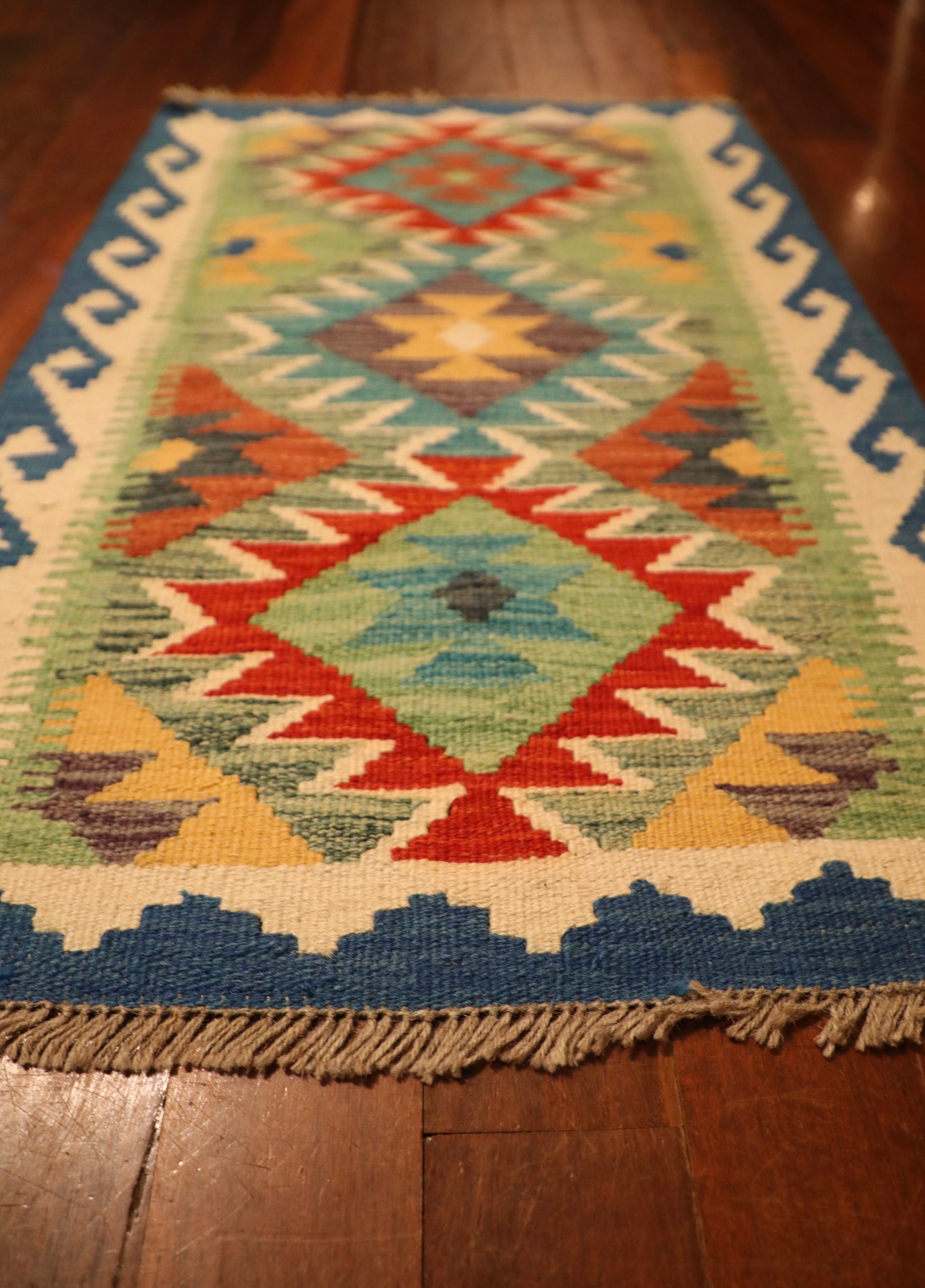 The Afghan Hand Woven Khyber Kilim - 56 X 90. Crafted using traditional vegetable dyed wool, and featuring traditional geometric designs. Colours, ocean blues, light greens, light blues, reds, beiges, creams, oranges and yellows. Size 56 X 90. Angle.