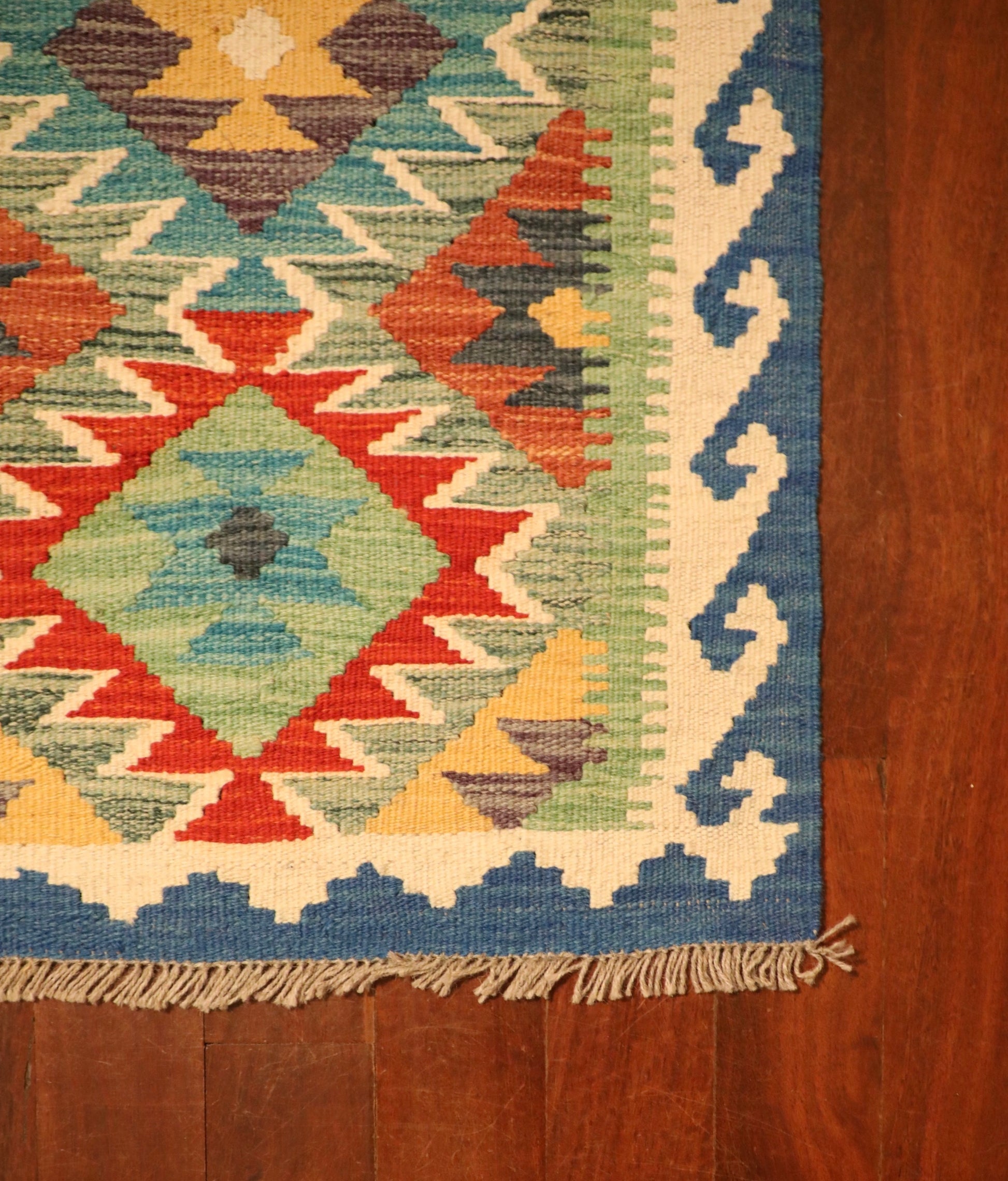 The Afghan Hand Woven Khyber Kilim - 56 X 90. Crafted using traditional vegetable dyed wool, and featuring traditional geometric designs. Colours, ocean blues, light greens, light blues, reds, beiges, creams, oranges and yellows. Size 56 X 90. Corner.