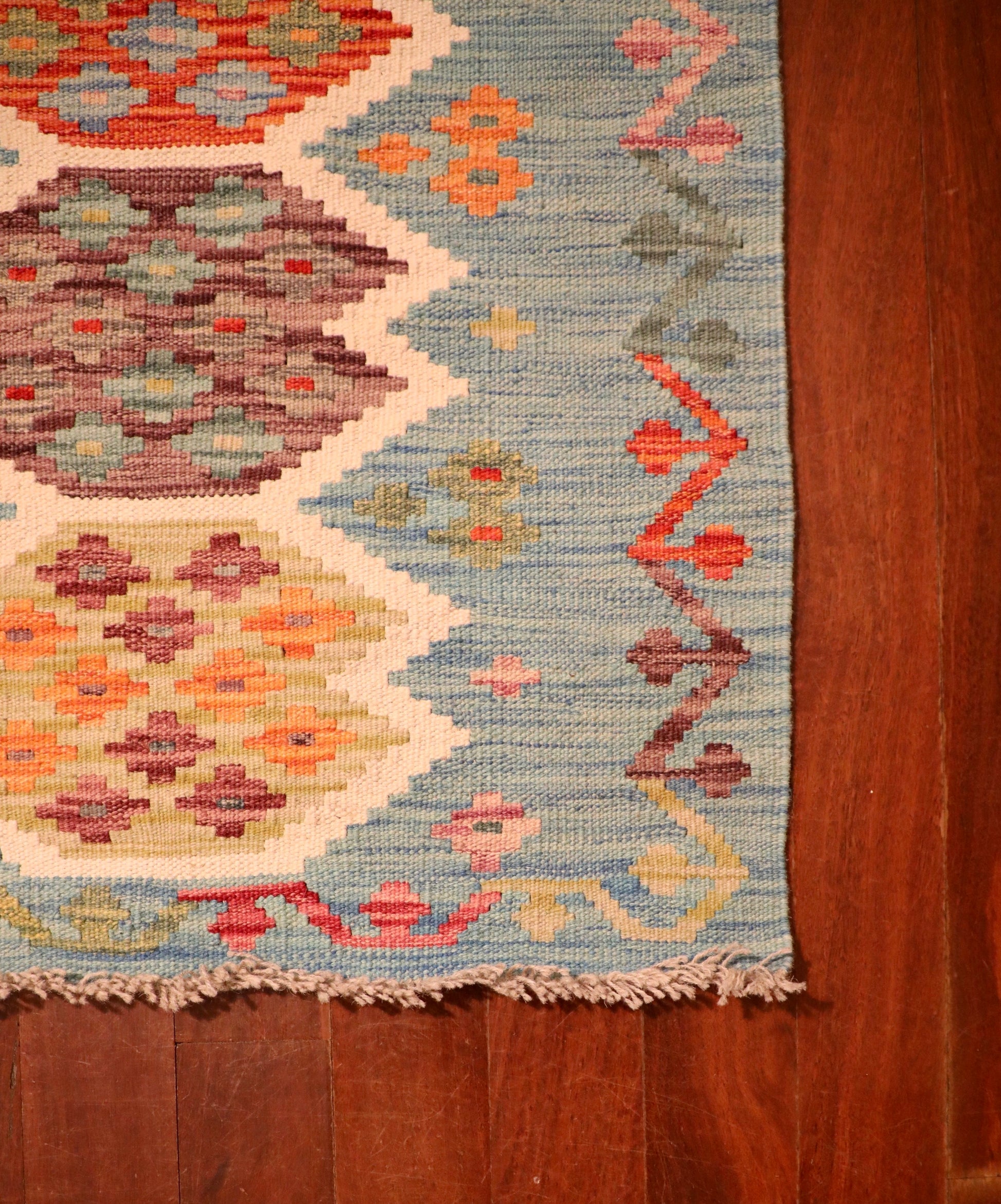 The Afghan Hand Woven Khyber Kilim - 68 X 92. Crafted using traditional vegetable dyed wool, and featuring traditional geometric designs. Colours, teal green, light blues, reds, beiges, creams, oranges and yellows. Size 68 X 92. Corner.