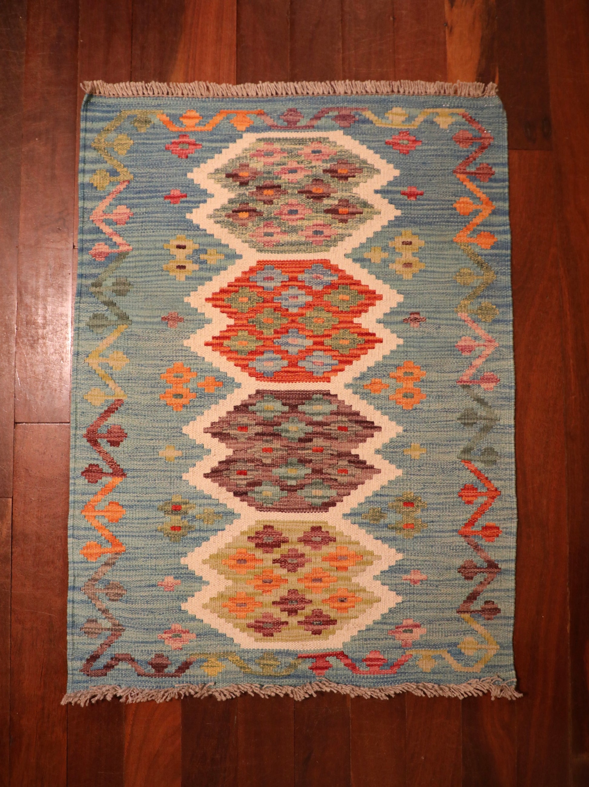 The Afghan Hand Woven Khyber Kilim - 68 X 92. Crafted using traditional vegetable dyed wool, and featuring traditional geometric designs. Colours, teal green, light blues, reds, beiges, creams, oranges and yellows. Size 68 X 92. Top.