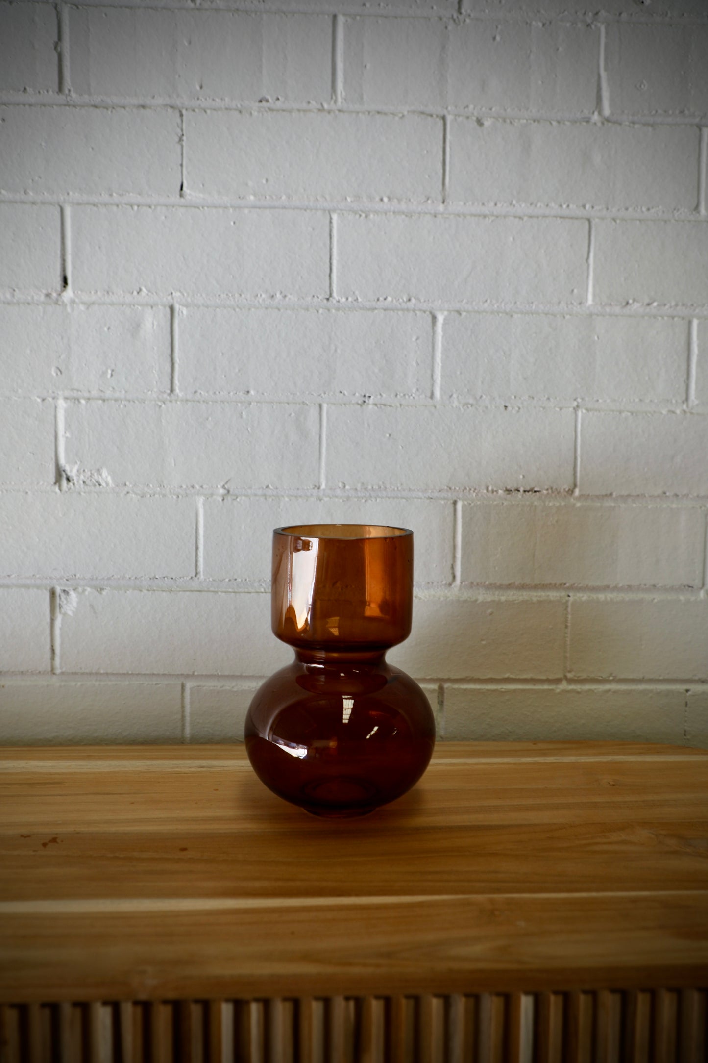 The Mallory Glass Vase,  a modern/contemporary designed piece. Features a bulbed bottom and a cylindrical top. Colour, Amber. Measures 14 Diameter X 20 Height. Side.