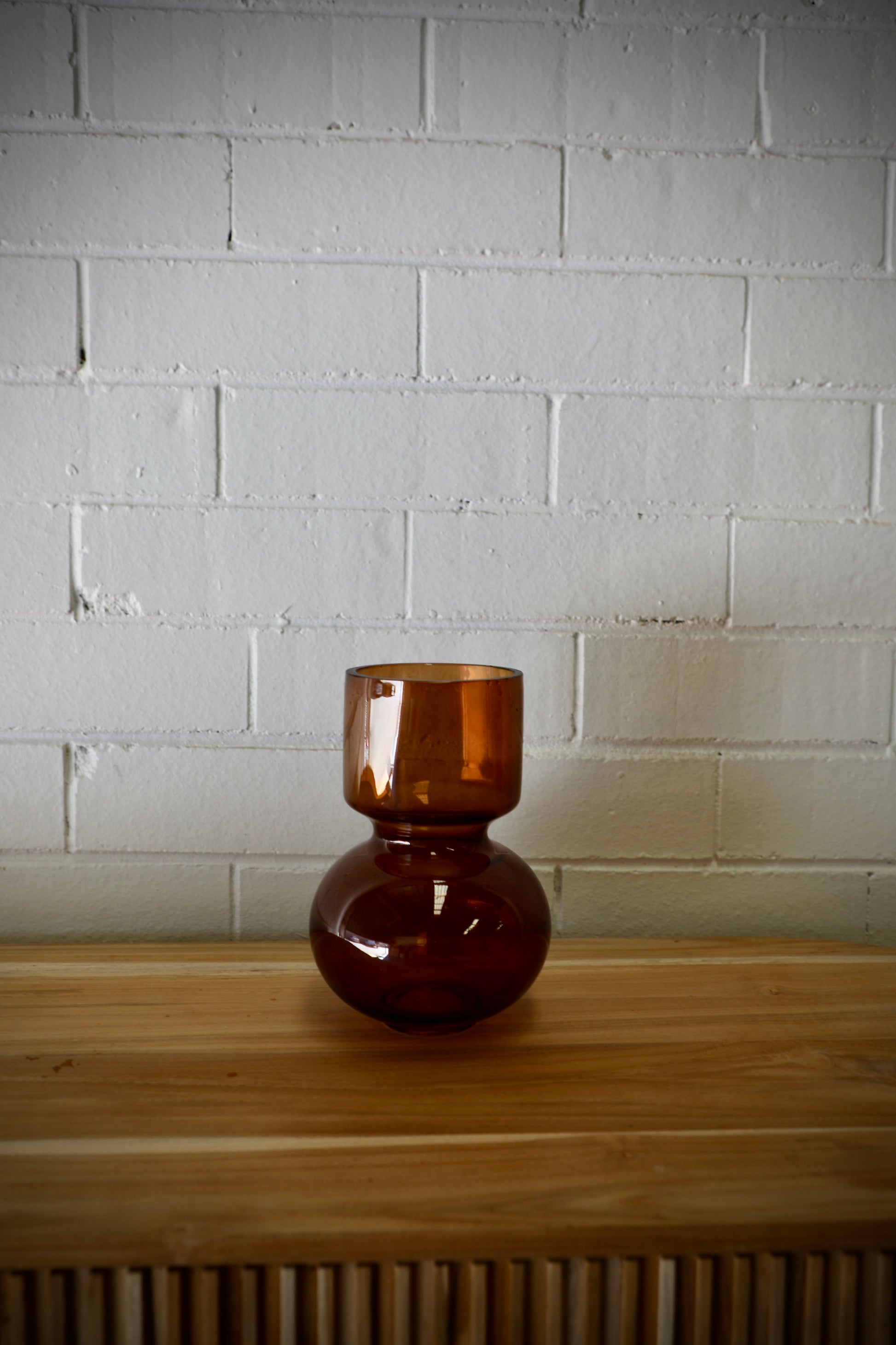 The Mallory Glass Vase,  a modern/contemporary designed piece. Features a bulbed bottom and a cylindrical top. Colour, Amber. Measures 14 Diameter X 20 Height. Side.
