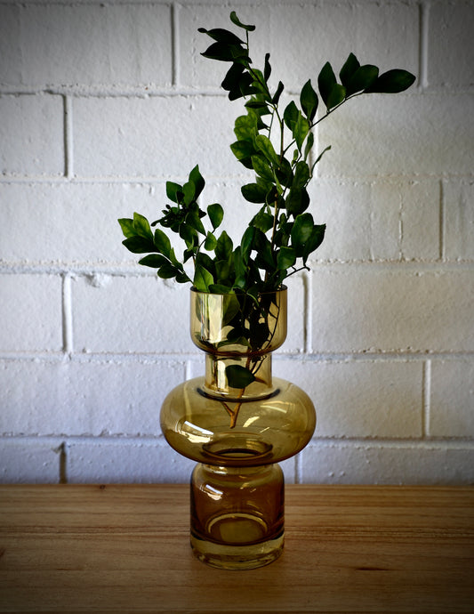 The Marte Glass Vase is a modern/contemporary piece. Featuring a cylindrical Bottom and top with a bulbed middle. Colour Amber. Measures 13 Diameter X 20 Height. Styled.