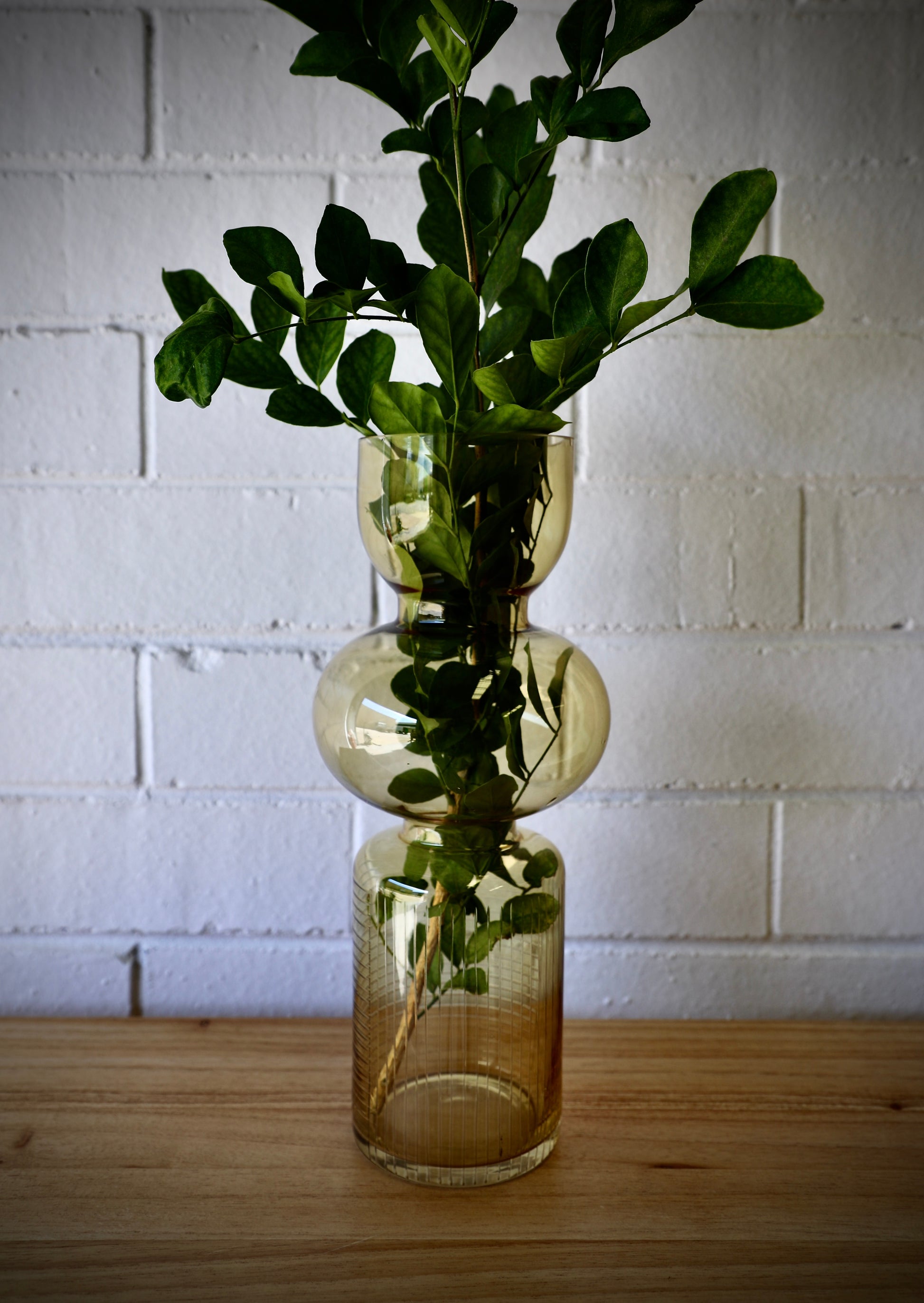 The Matar Glass Vase features a 3 column design. A cylindrical textured bottom, with bulbed middle and bowled open top. Colour Amber. Measures 13 Diameter X 30 Height. Styled.