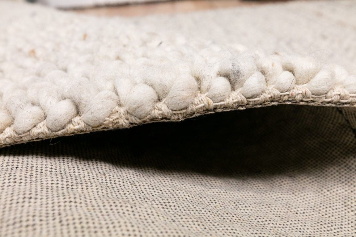 Oslo Loop is a textured hand woven, piled loop wool rug. Colours white with grey,  black and brown accents. Sizes 155 X 225, 200 X 290, 240 X 320 and 300 X 400. Side.