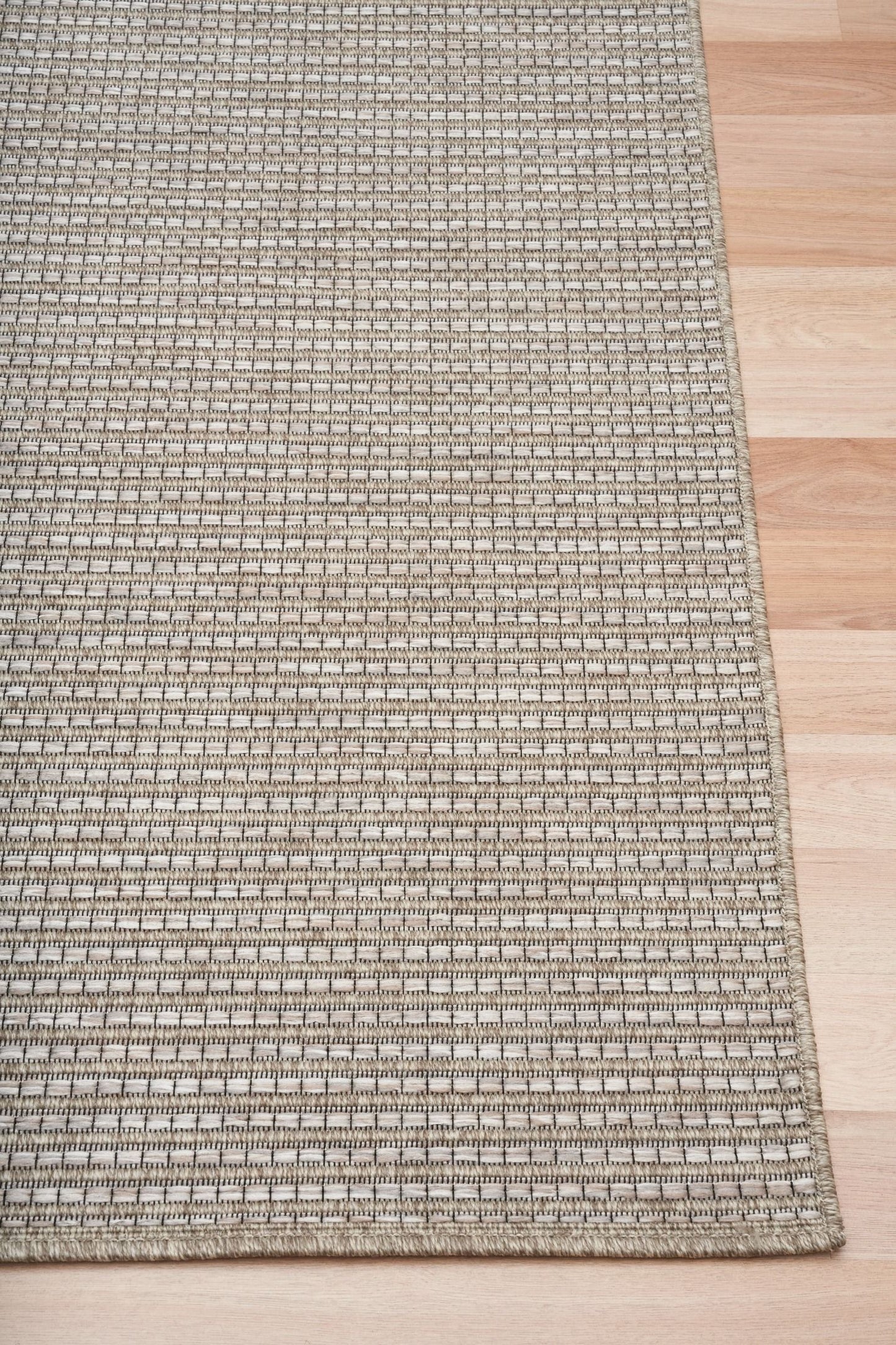 The Patio Basket Straw indoor/outdoor rug featuring neutral tones and a modern designed pattern, power-loomed from UV-stabilised polypropylene for lasting durability. Colours Greys, Beiges and hints of light grey. 3 sizes. Corner.