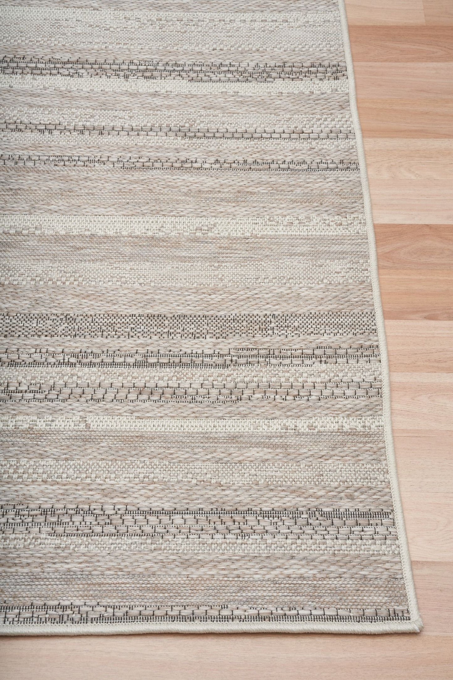The Patio Linear Linen indoor/outdoor rug featuring neutral tones and a subtle textured pattern, power-loomed from UV-stabilised polypropylene for lasting durability. Colours, Linen, Beiges and hints of black. 3 sizes. Corner.