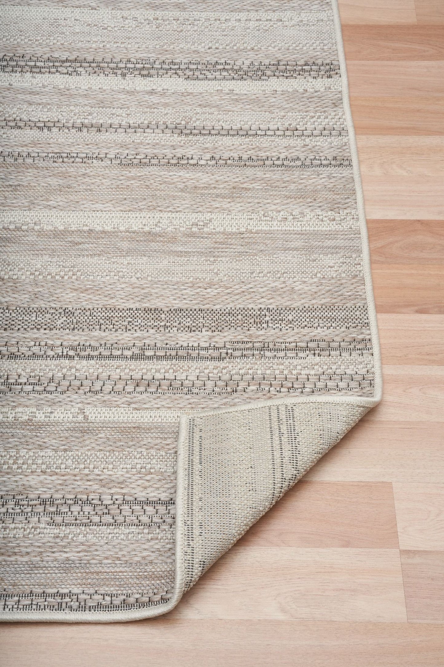 The Patio Linear Linen indoor/outdoor rug featuring neutral tones and a subtle textured pattern, power-loomed from UV-stabilised polypropylene for lasting durability. Colours, Linen, Beiges and hints of black. 3 sizes. Fold.