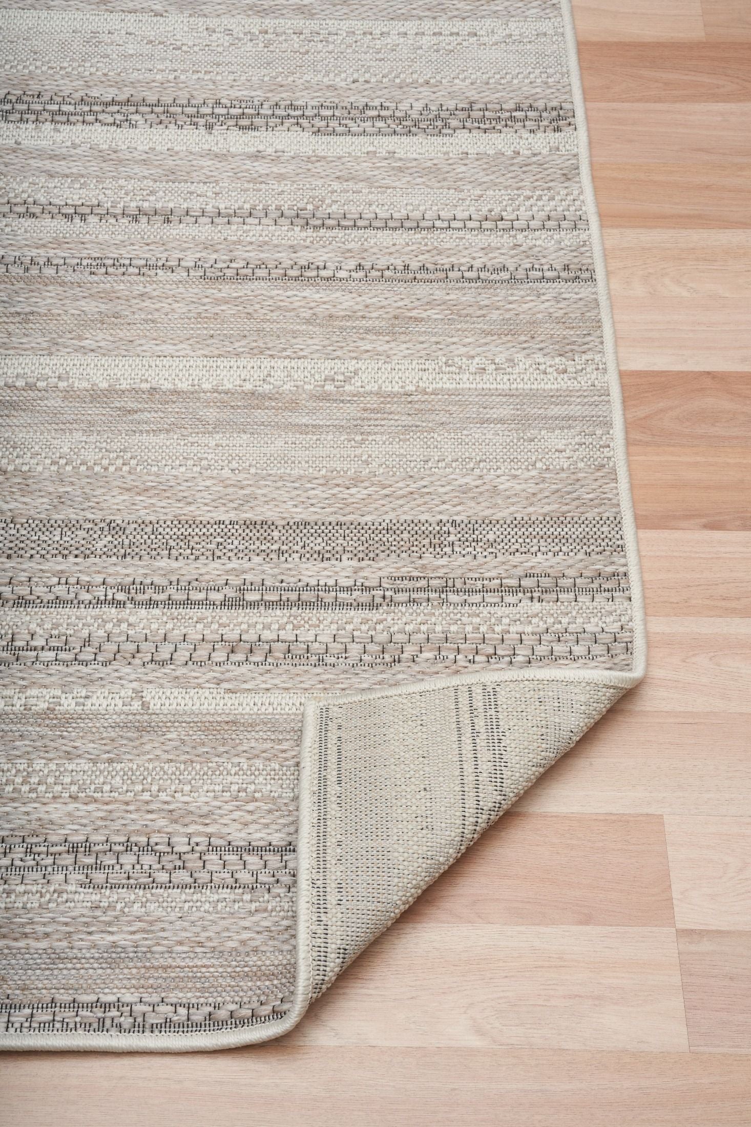 The Patio Linear Linen indoor/outdoor rug featuring neutral tones and a subtle textured pattern, power-loomed from UV-stabilised polypropylene for lasting durability. Colours, Linen, Beiges and hints of black. 3 sizes. Fold.