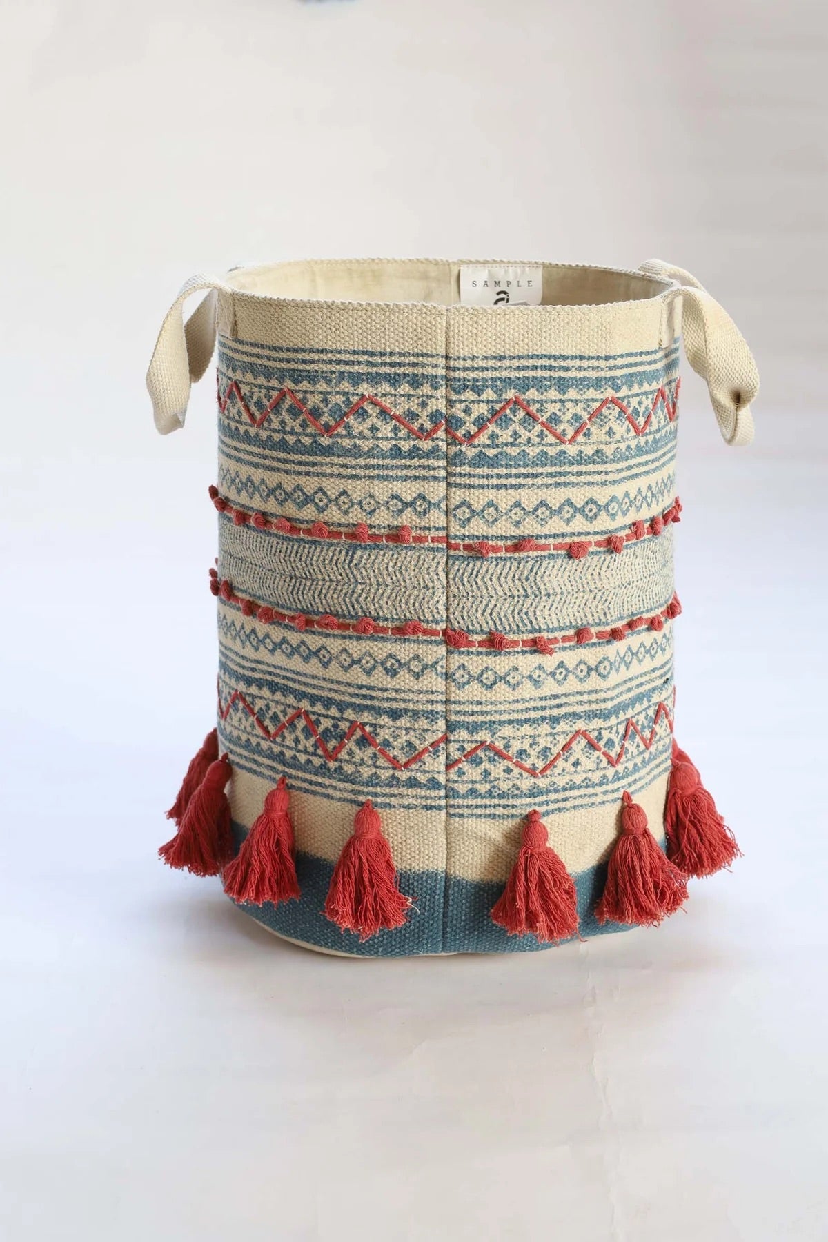 The Redwood Cotton Block Print Basket, showcases a bold motif block print design and 2 handles. Featuring an interior cotton lining and an outer cotton textured cover with red tassels.  Colours, cream, blue,  and red. Size 400 height X 350 diameter. Side Plain.