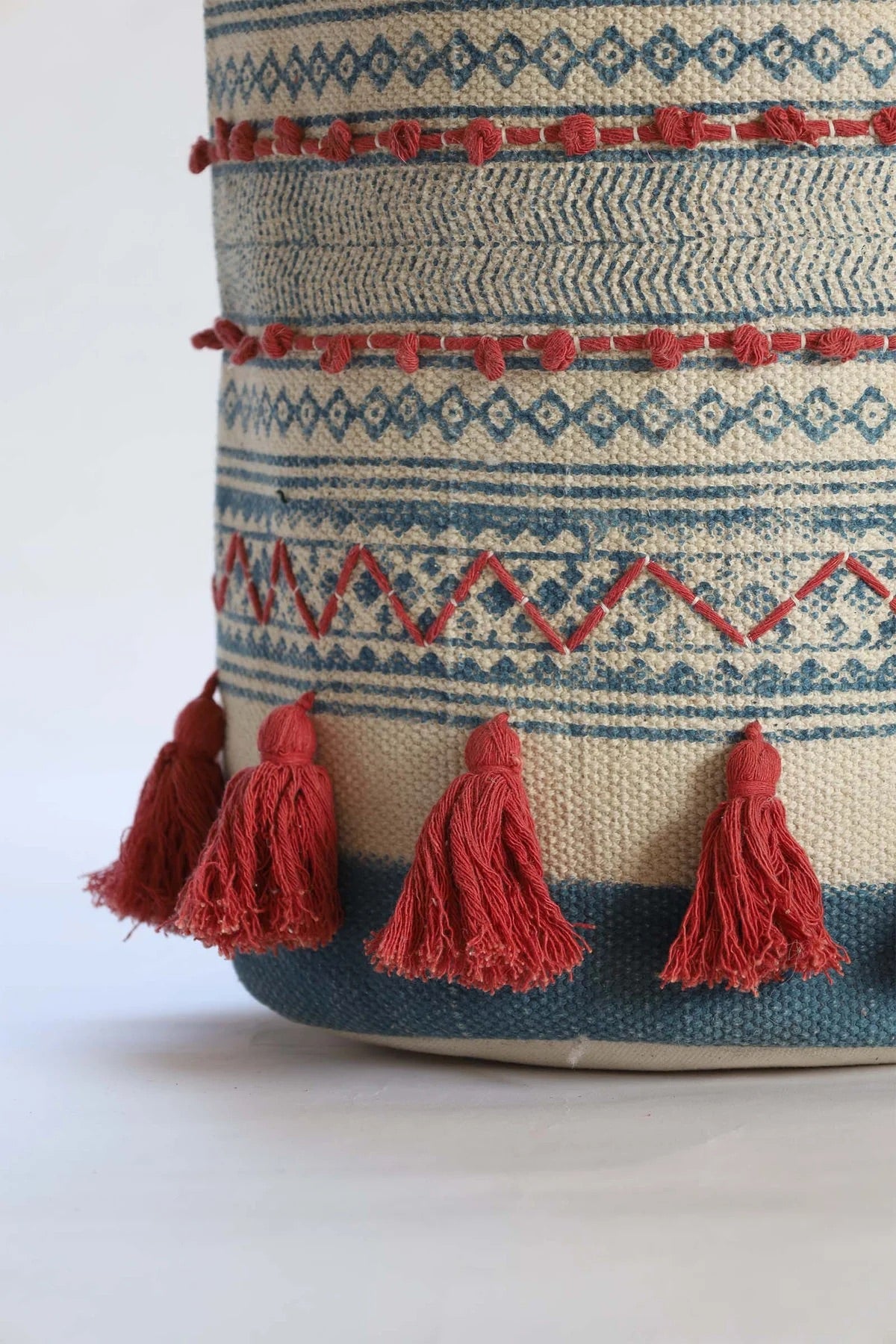 The Redwood Cotton Block Print Basket, showcases a bold motif block print design and 2 handles. Featuring an interior cotton lining and an outer textured cotton cover with red tassels.  Colours, cream, blue,  and red. Size 400 height X 350 diameter. Bottom corner.