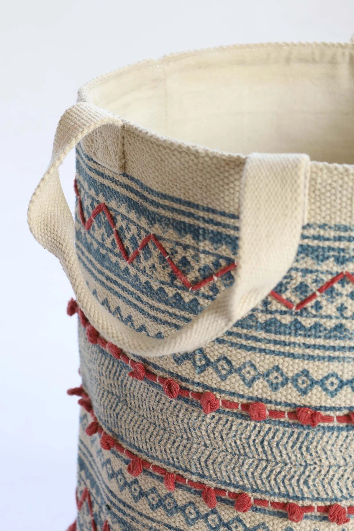 The Redwood Cotton Block Print Basket, showcases a bold motif block print design and 2 handles. Featuring an interior cotton lining and an outer textured cotton cover with red tassels.  Colours, cream, blue,  and red. Size 400 height X 350 diameter. Top corner.