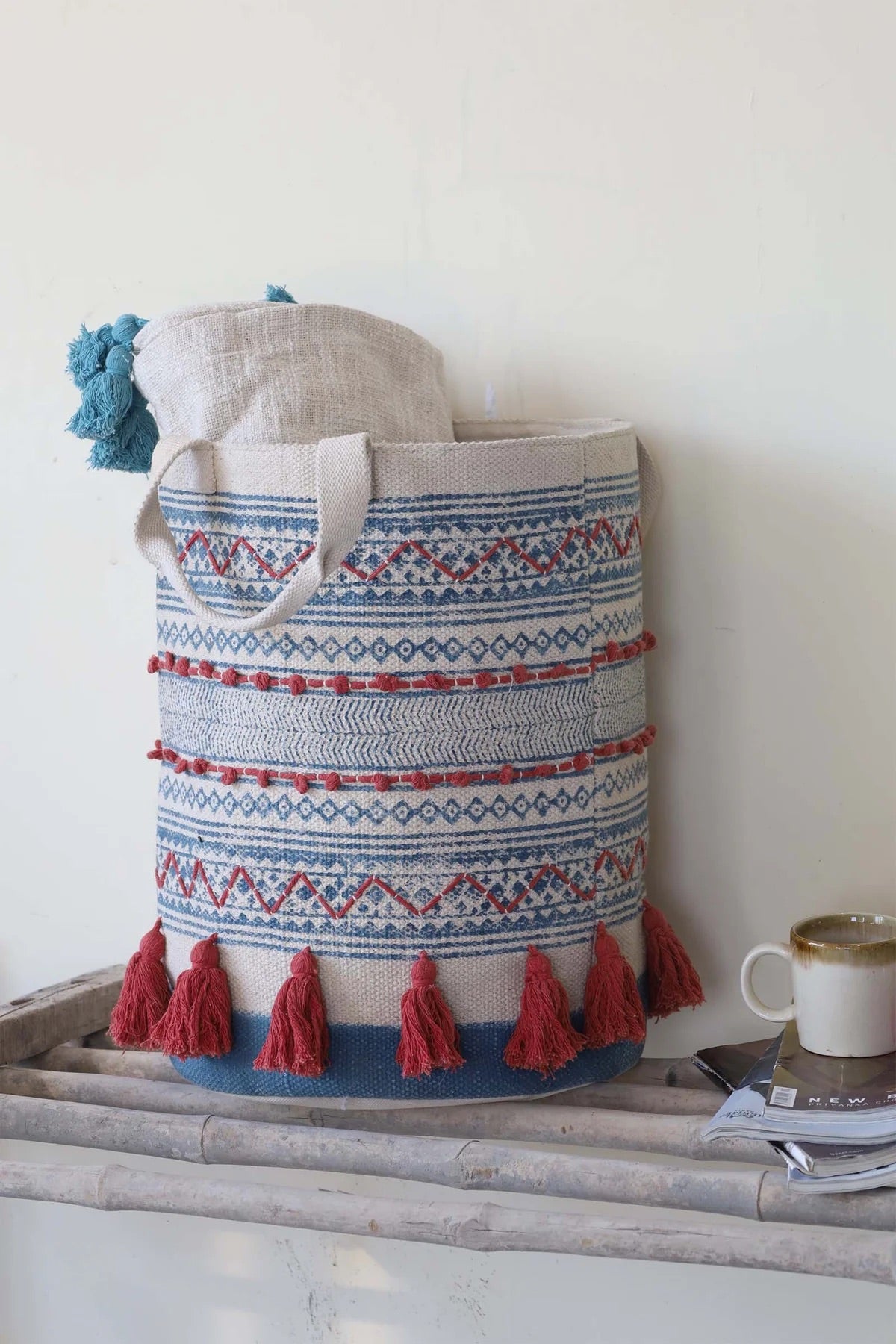 The Redwood Cotton Block Print Basket, showcases a bold motif block print design and 2 handles. Featuring an interior cotton lining and an outer cotton textured cover with red tassels.  Colours, cream, blue,  and red. Size 400 height X 350 diameter. Front Styled.