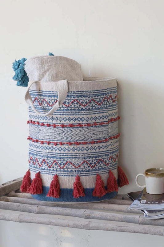 The Redwood Cotton Block Print Basket, showcases a bold motif block print design and 2 handles. Featuring an interior cotton lining and an outer cotton textured cover with red tassels.  Colours, cream, blue,  and red. Size 400 height X 350 diameter. Front Styled.