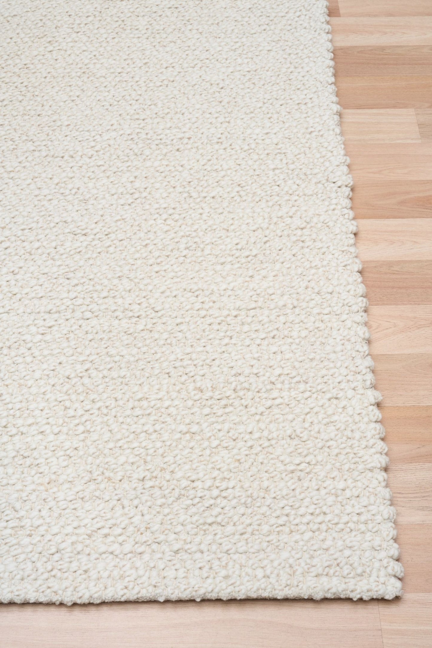 Sahara Ivory Rug – hand woven 100% wool rug in soft neutral tones with a textured finish, available in three sizes, styled for modern and coastal homes. Corner.